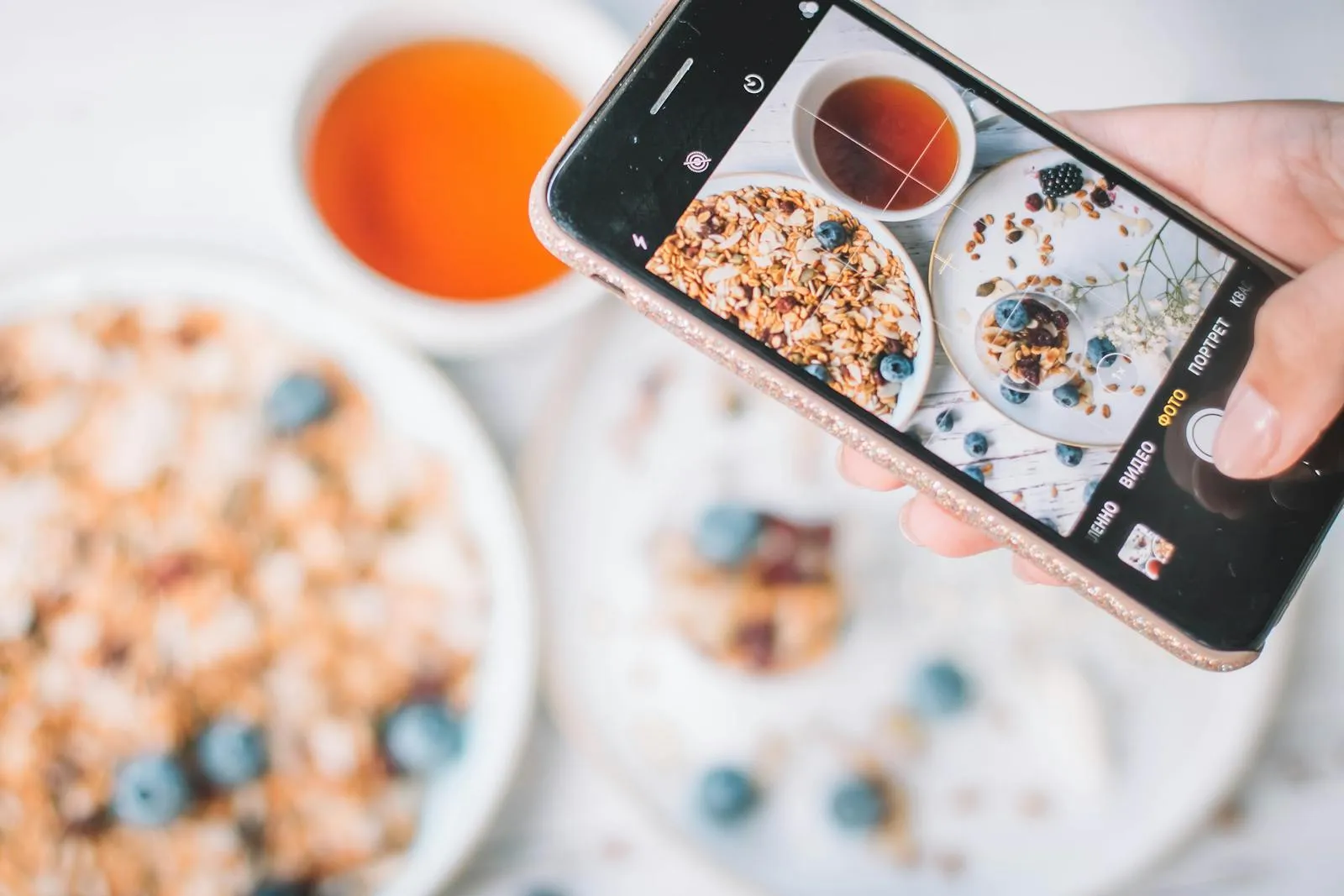 A smartphone captures a healthy breakfast bowl with blueberries and a cup of tea — a typical AI-logging workflow