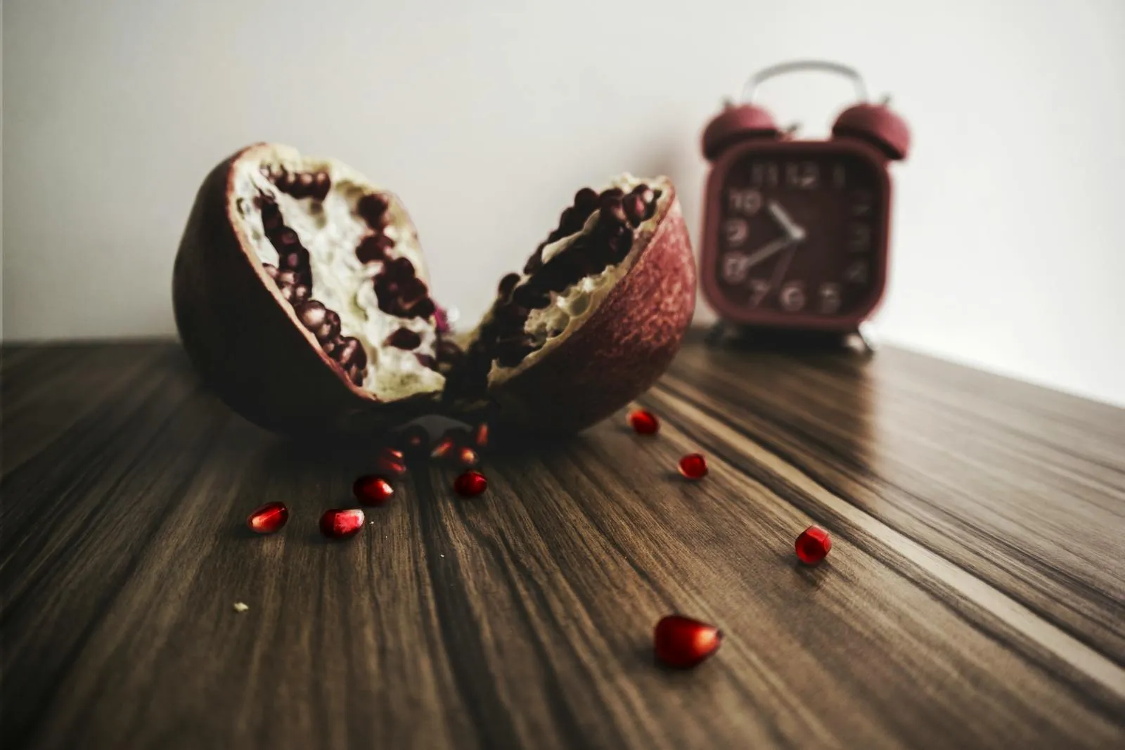 A pomegranate next to a red retro alarm clock on a rustic surface — visual of time-restricted eating