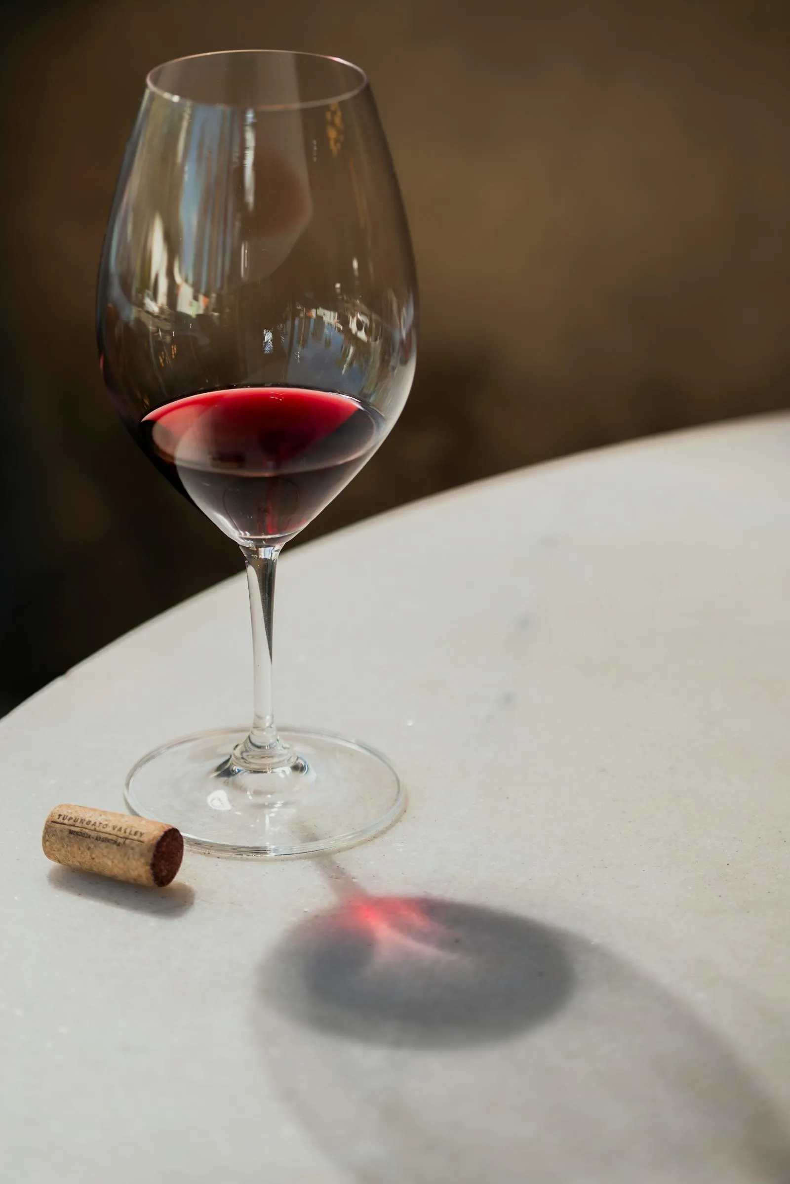 An elegant glass of red wine sits on a marble table in soft indoor light