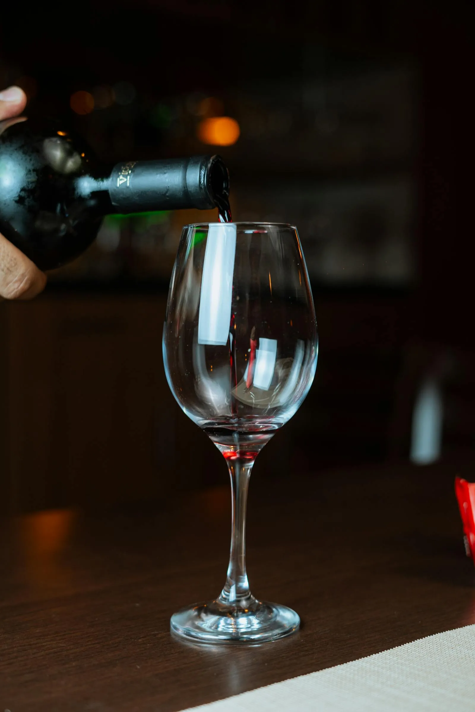 Red wine being poured into a glass in a warm indoor setting